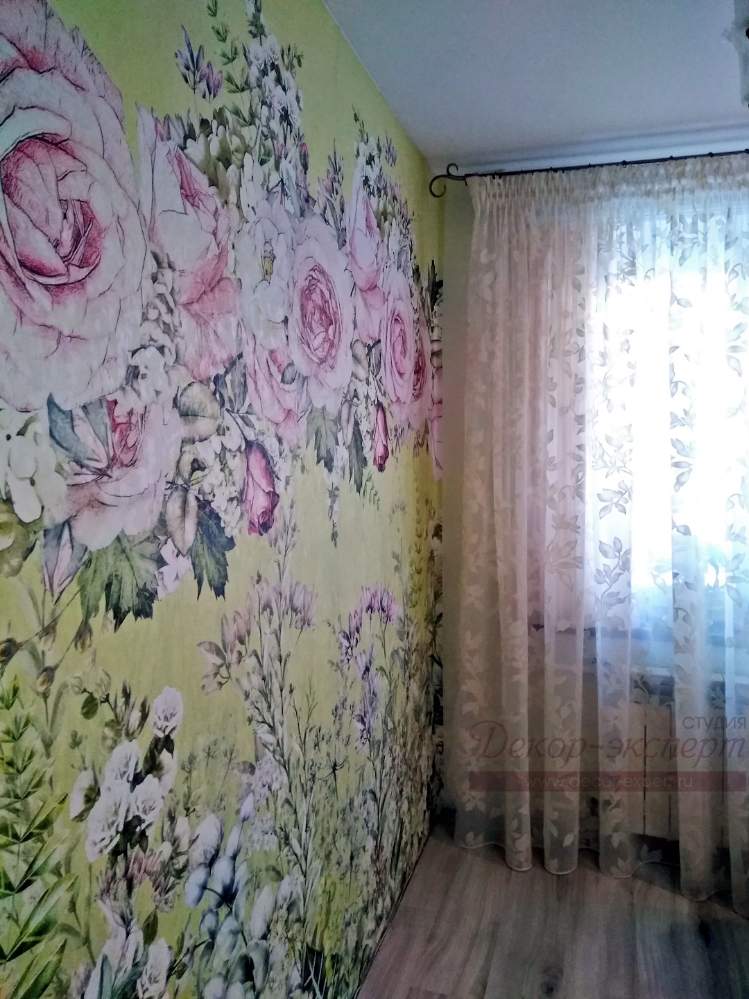 Фотообои с розами на стене кухни и тюль деворе на окне при дневном освещении.